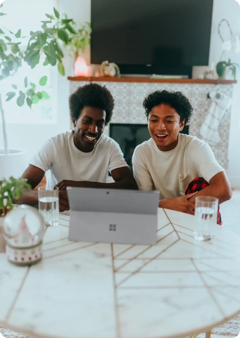 Two young men smiling at a laptop at a kitchen table