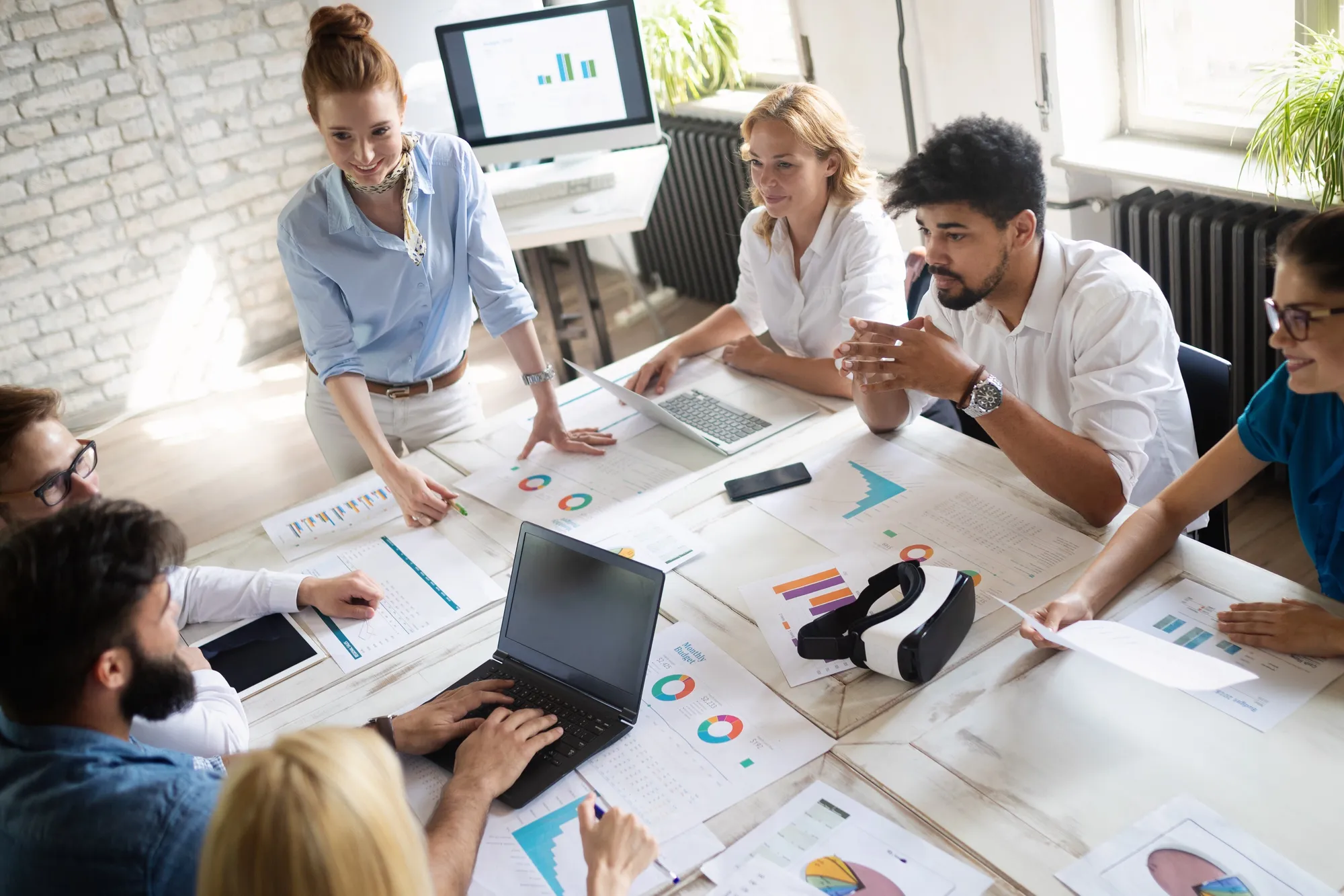 Team around a meeting table covered with charts, laptops and a VR headset