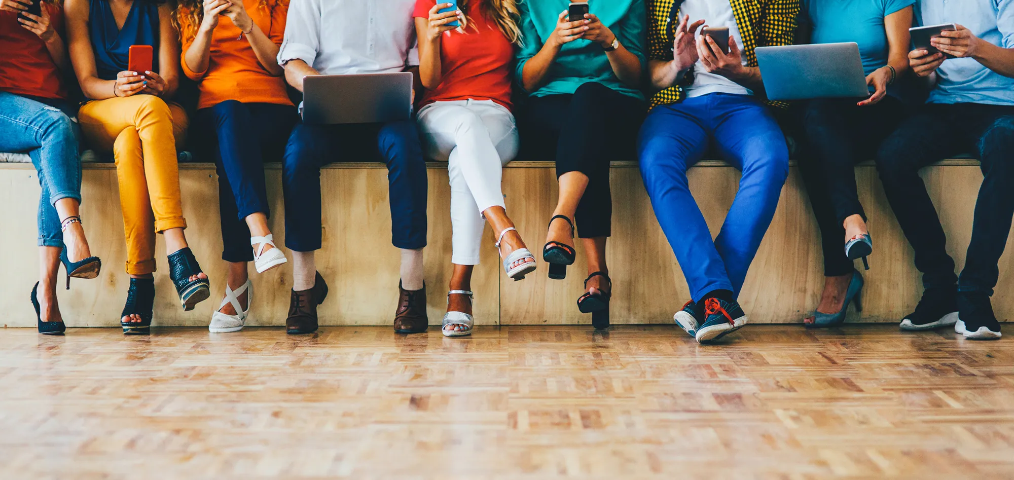 Row of people sitting on a bench, each looking at a phone, tablet or laptop