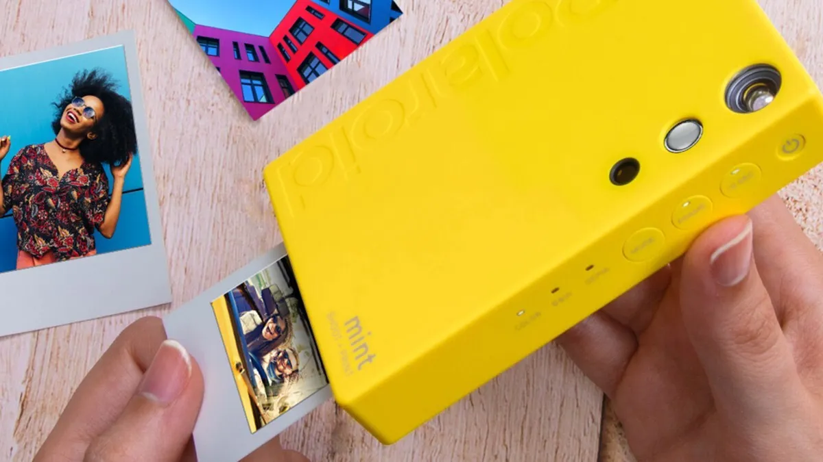 Hand holding a yellow Polaroid Mint instant camera as it prints a photo