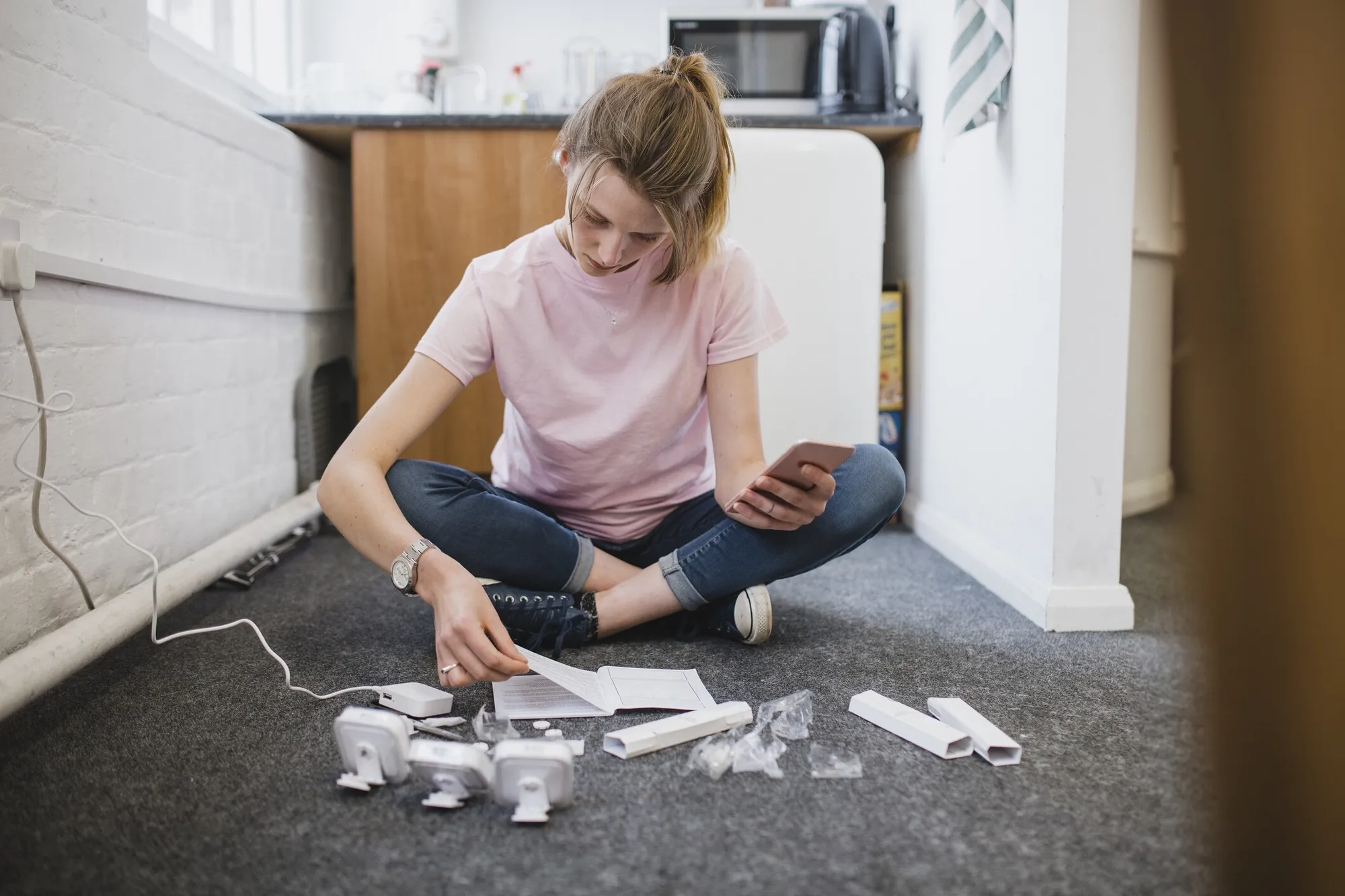 Woman sitting on the floor reading setup instructions next to the parts of a new device