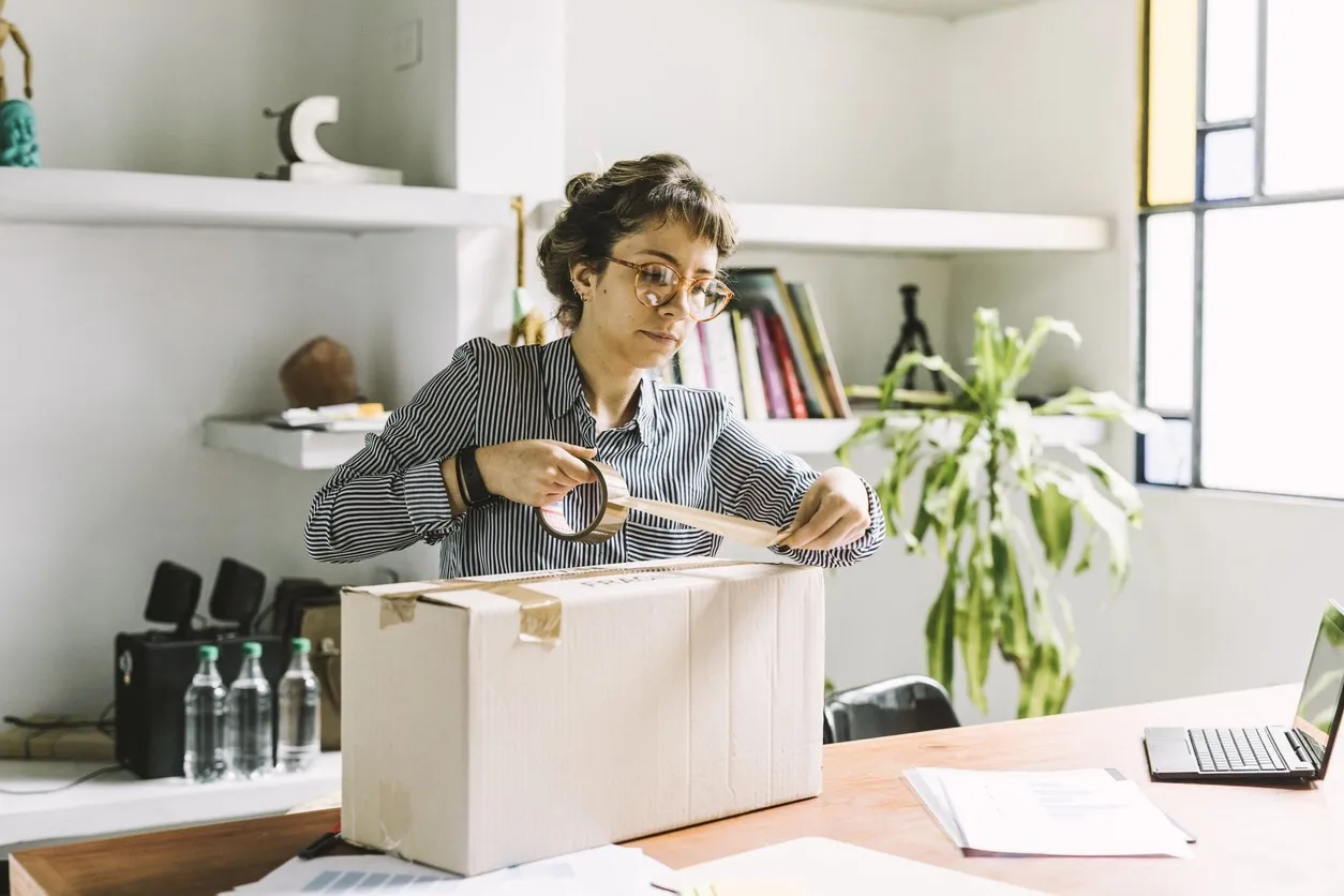 Woman taping up a cardboard box at her desk