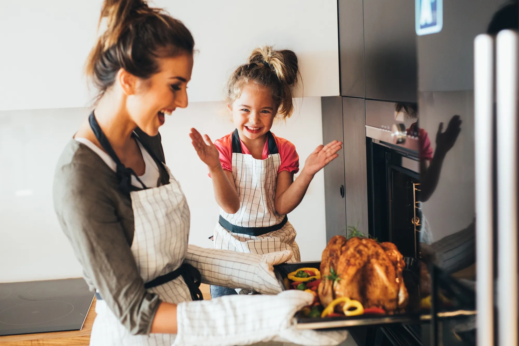 Mother and daughter cheering as a roast chicken comes out of the oven
