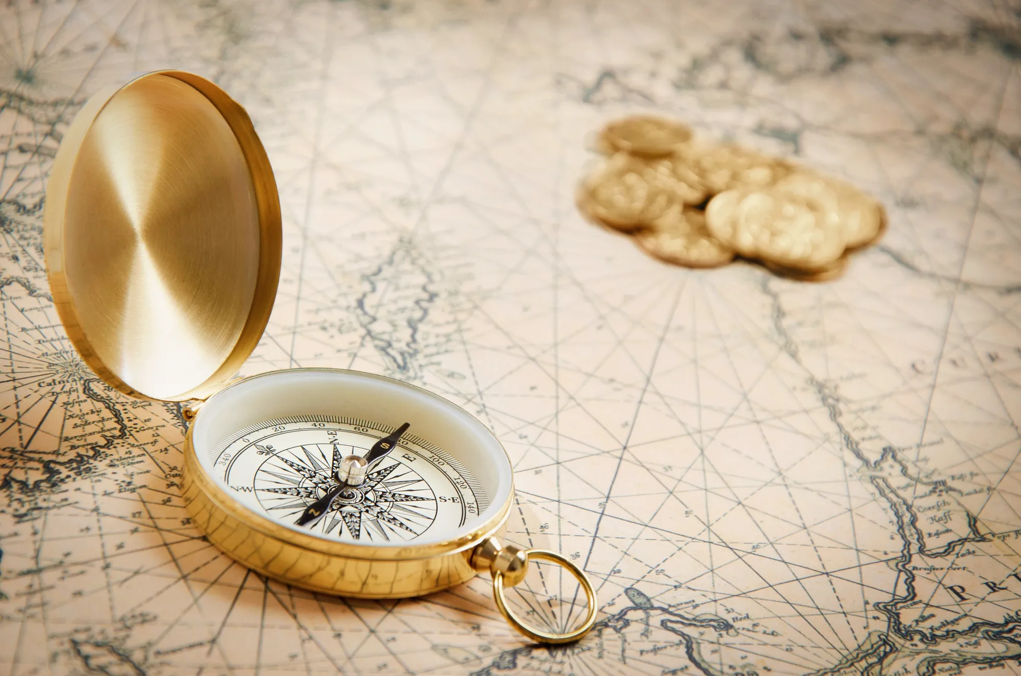 Brass compass and gold coins on an old map