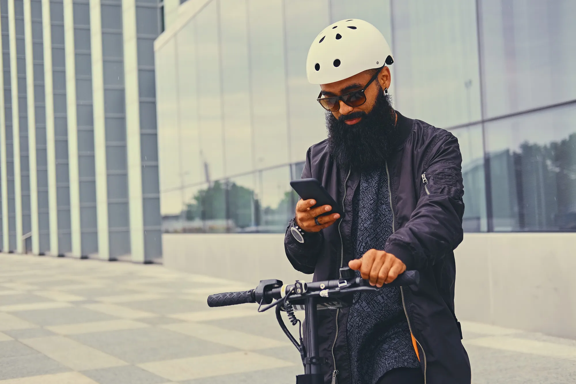 Man in a helmet checking his phone while riding an electric scooter